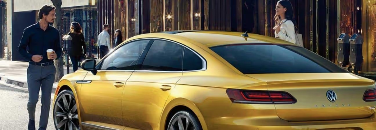 man holding a coffee walking up to his 2019 Volkswagen Arteon