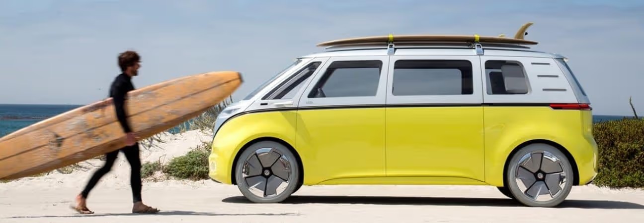 surfer walking with surfboard to his Volkswagen parked in front of the ocean